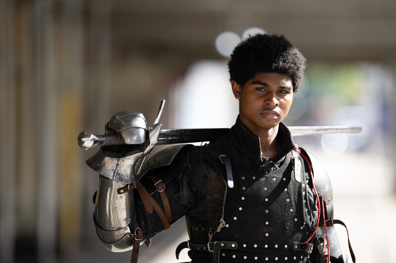 Portrait of a young man with textured natural hair wearing a black studded leather jacket, carrying professional camera equipment over his shoulder