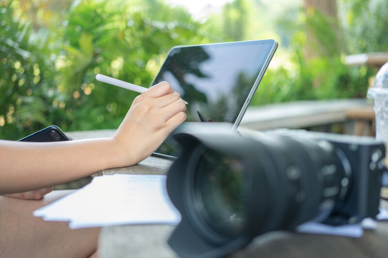 Photographer using stylus on tablet with professional camera in foreground
