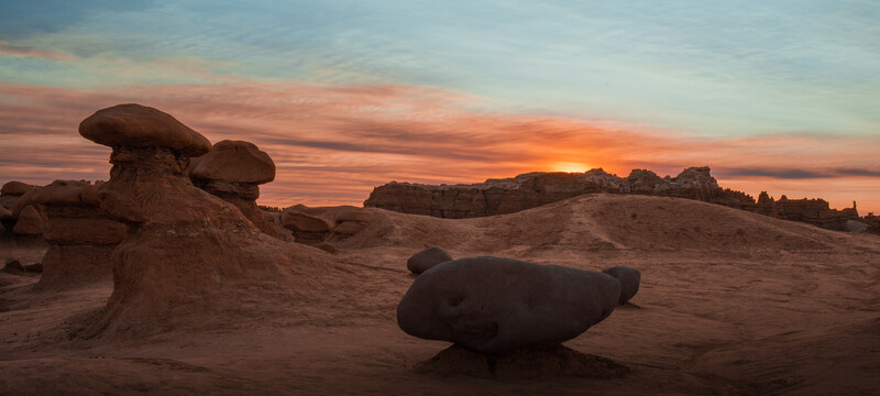 Desert rock formations silhouetted against vibrant orange sunset sky