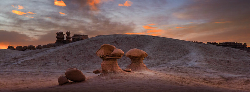 Mushroom-shaped rock formations silhouetted against dramatic orange sunset sky in desert landscape