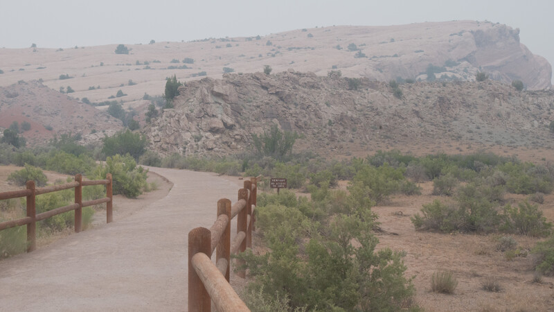 Rustic wooden fence railing along a dusty path with arid hillside landscape