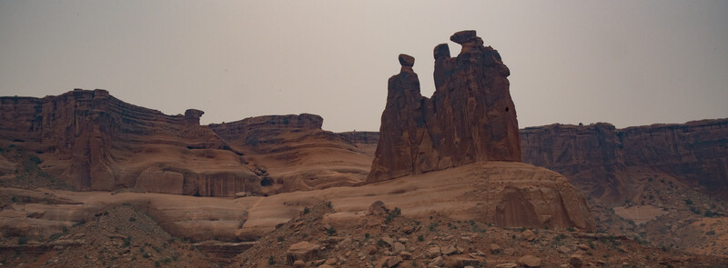 Towering red sandstone formations rise from desert landscape under hazy sky