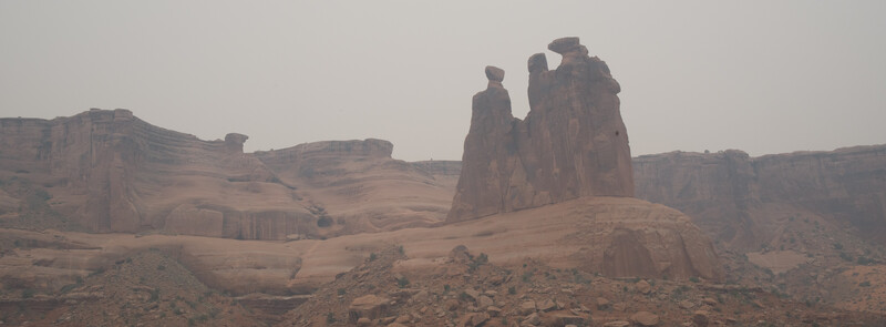 Towering red rock formations rise from desert landscape under hazy sky