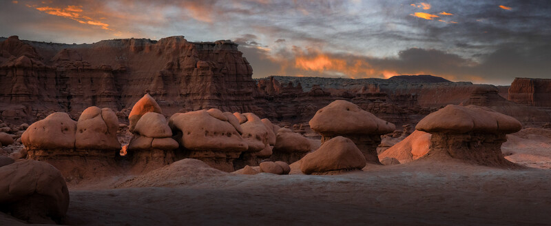 Desert landscape at sunset with distinctive rounded boulder formations and layered rock formations under dramatic orange and gray clouds