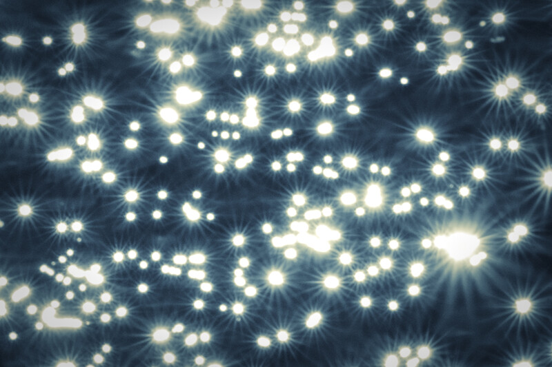 Abstract bokeh light pattern with bright white points and starburst lens flares against dark blue background