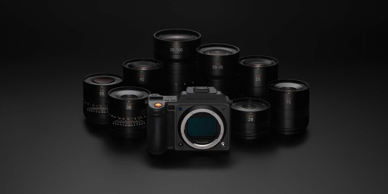 Mirrorless camera body surrounded by eight black telephoto and zoom lenses arranged in a circular composition