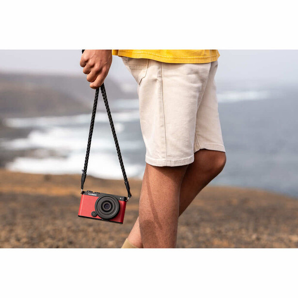 Person holding a compact red camera with black strap at coastal overlook