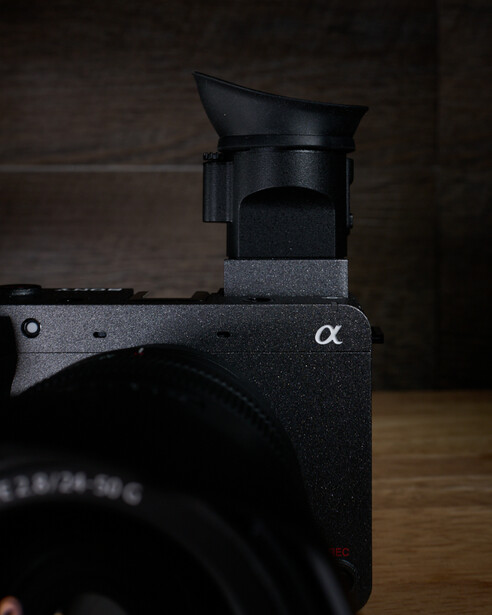 Sony Alpha mirrorless camera with electronic viewfinder mounted on top, displayed against dark background on wooden surface
