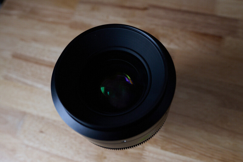 Black telephoto lens with front element visible, shot from above on wooden floor
