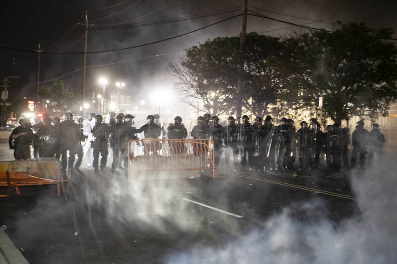 Riot police in formation facing tear gas clouds during nighttime street protest