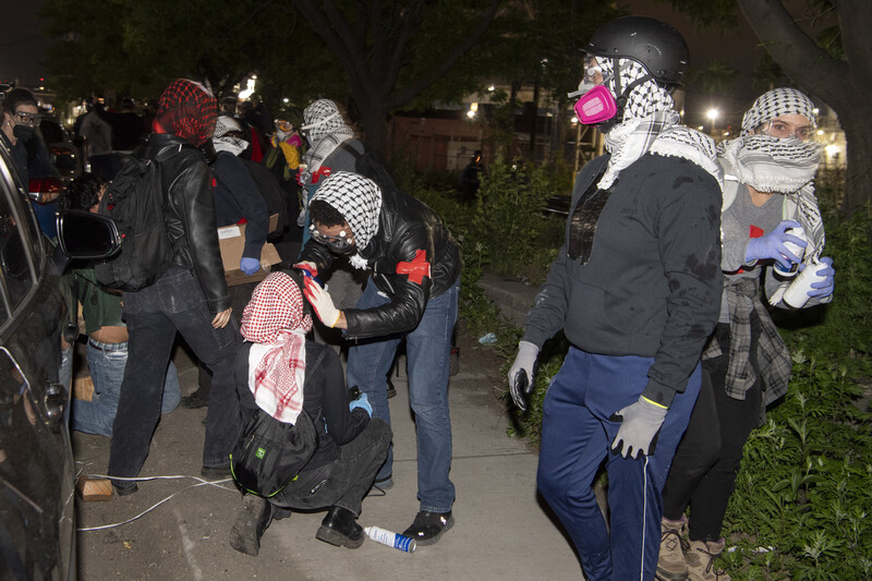 Group of people wearing keffiyehs and winter clothing gathered on a nighttime street during a protest or demonstration.