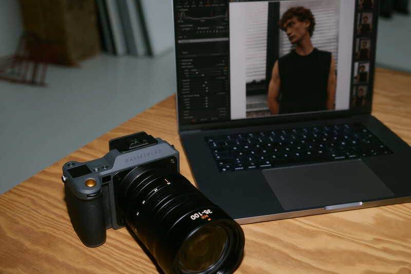 Mirrorless camera with telephoto lens on wooden desk next to laptop displaying photo editing software