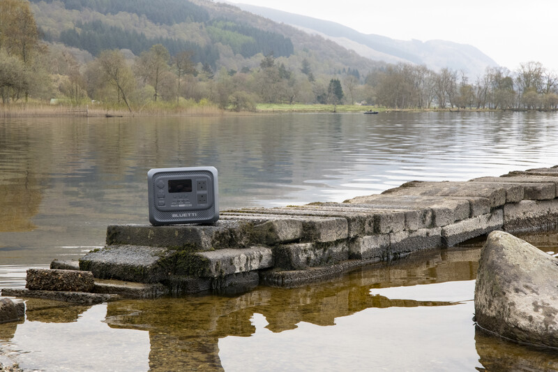 Portable power station on weathered stone blocks by a misty lake with forested mountains