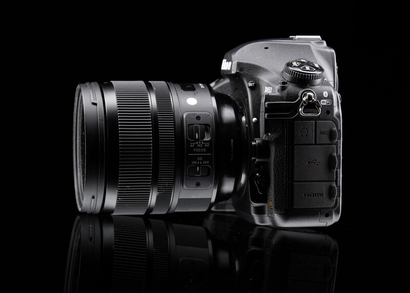 Mirrorless camera with attached standard zoom lens positioned on black reflective surface against dark background