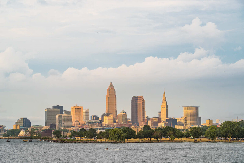 Cleveland skyline photographed across Lake Erie during golden hour with cumulus clouds