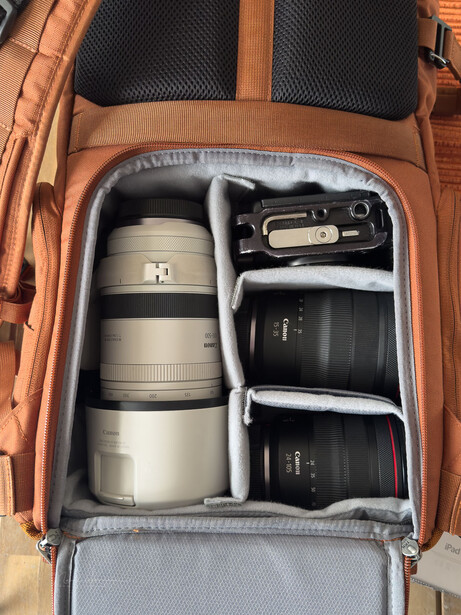 Orange camera backpack with organized lens compartments displaying telephoto and standard lenses