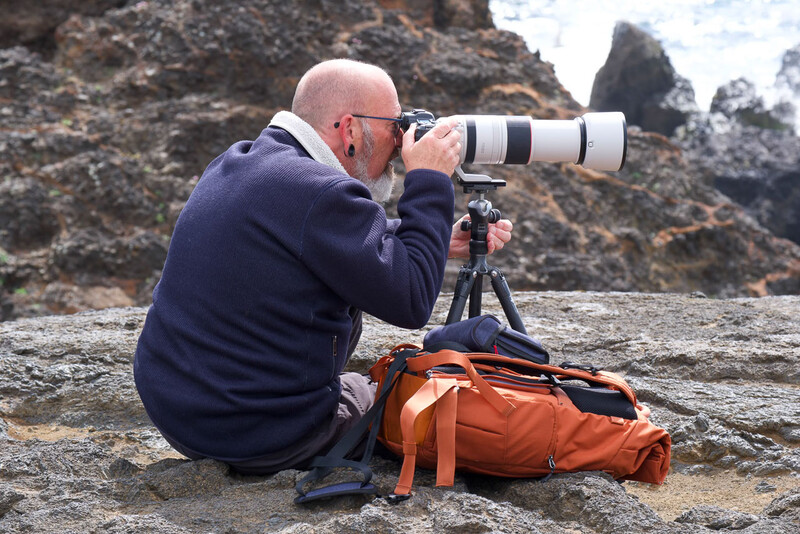 Photographer with telephoto lens mounted on tripod at rocky coastal location