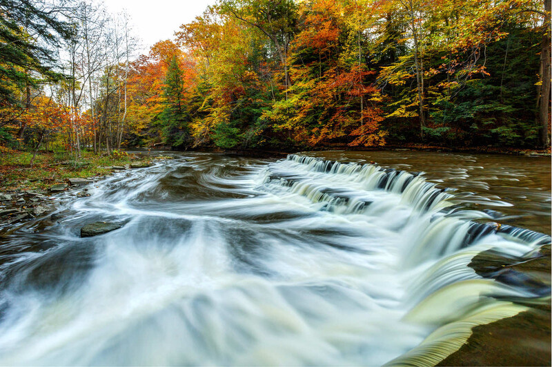 Cascading waterfall with silky water flow through autumn forest foliage