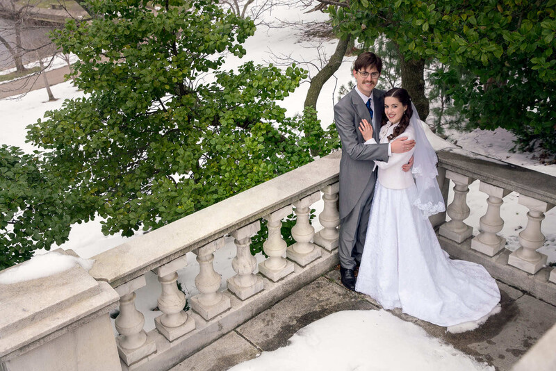 Bride and groom posing on a stone balustrade overlooking a coastal landscape with ivy-covered trees
