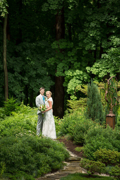 Bride and groom standing together on a garden path surrounded by lush green foliage and trees