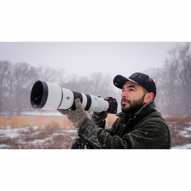 Photographer holding a white telephoto lens while shooting in snowy landscape