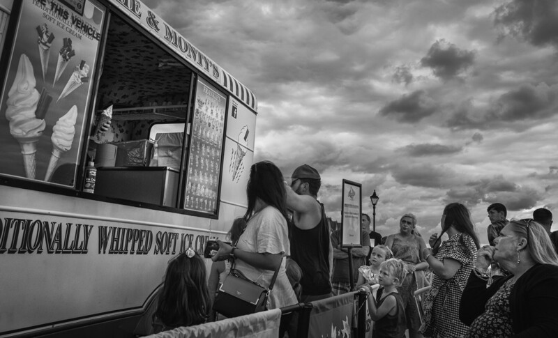 Customers queue at a food truck window against a dramatic cloudy sky