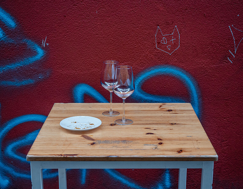 Wooden table with wine glasses and plate against maroon wall with blue graffiti