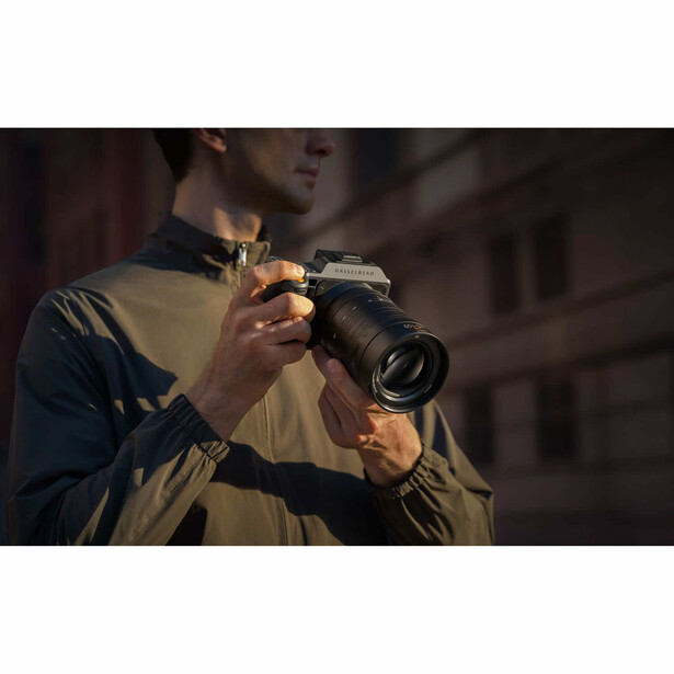 Photographer holding a DSLR camera up to his eye, composing a shot in low-light urban setting