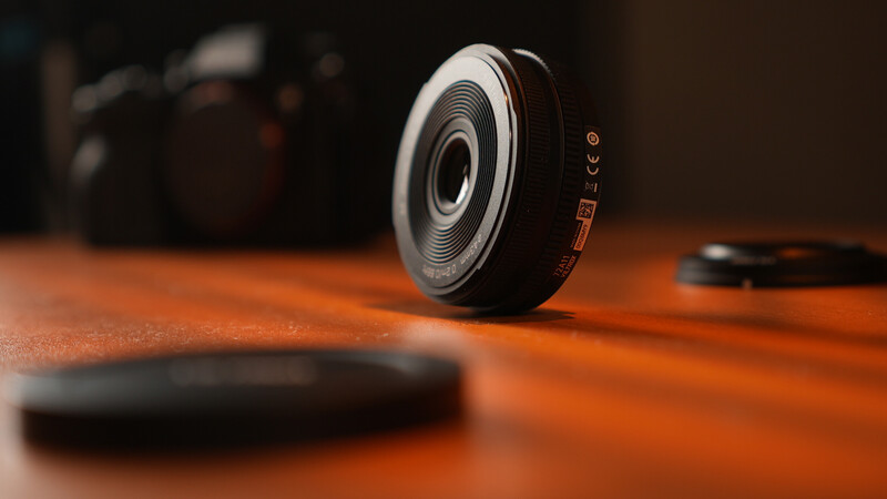 Compact camera lens displayed on wooden surface with shallow depth of field