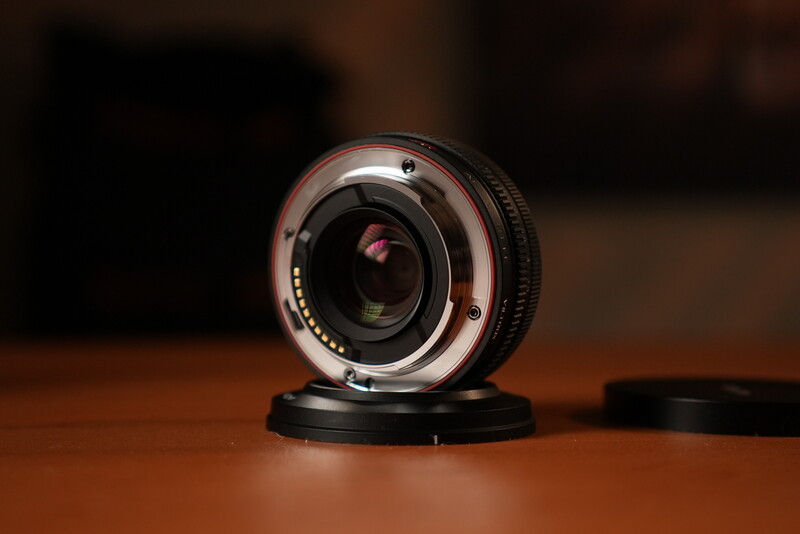 Vintage camera lens mounted on black base, rear element visible, wooden surface background