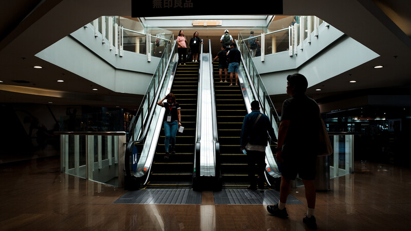 Symmetrical photograph of two escalators in a modern shopping mall with passengers ascending and descending