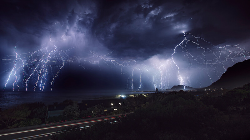 Dramatic lightning storm with multiple branching bolts illuminating dark clouds above a distant town at night