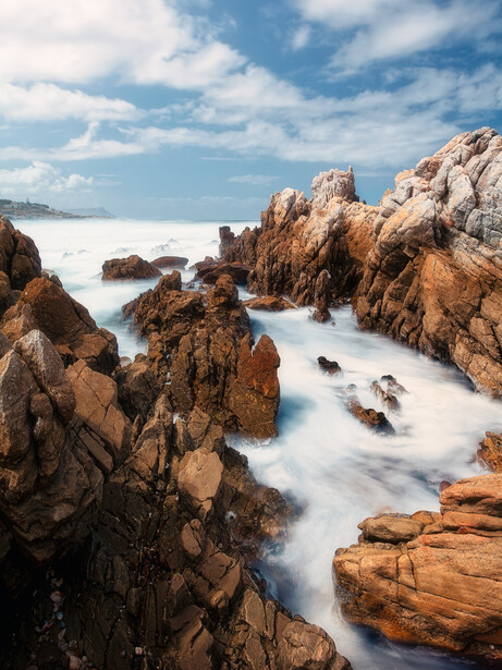 Rocky coastal landscape with long exposure waves flowing through boulder formations