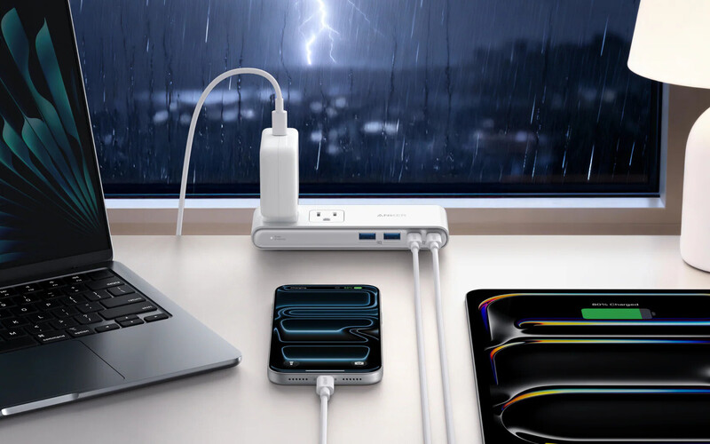 Desk setup with laptop, smartphone, and external hard drives connected to a multi-port USB hub during a thunderstorm