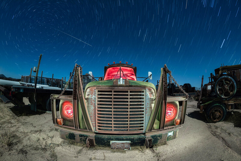 Vintage truck with red cab and green grille photographed head-on at night with star trails overhead