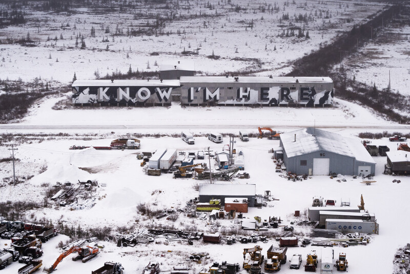 Aerial view of snowy industrial site with "KNOW I'M HERE" text visible