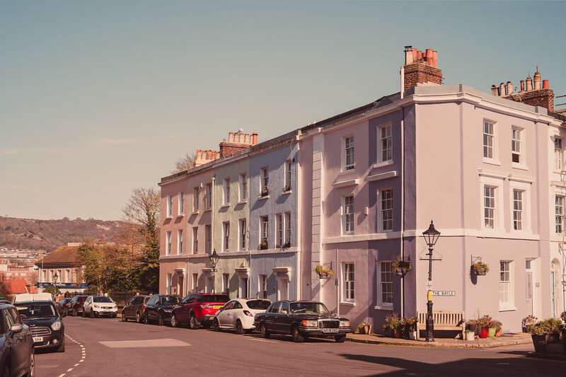 Pastel-colored Georgian townhouses with parked cars on a tree-lined street