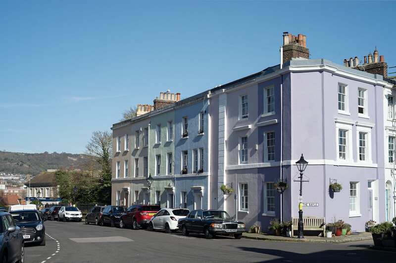 Pastel-colored Georgian townhouses with parked cars on a tree-lined street