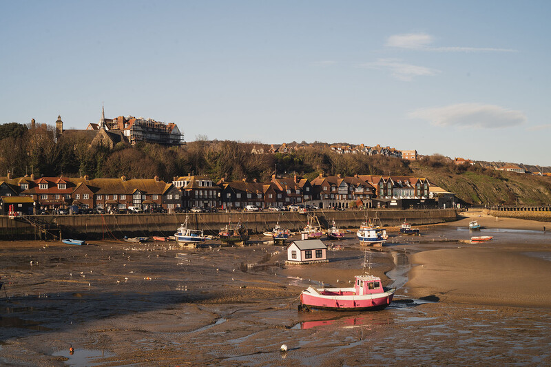 Red and white fishing boat moored on mudflats with seaside village and hilltop castle in background