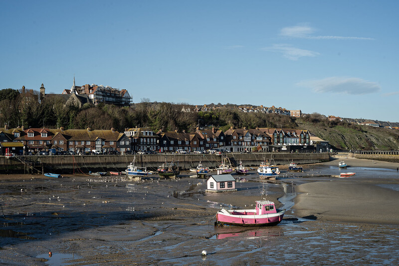 Coastal town with castle on hilltop overlooking tidal harbor with beached boats