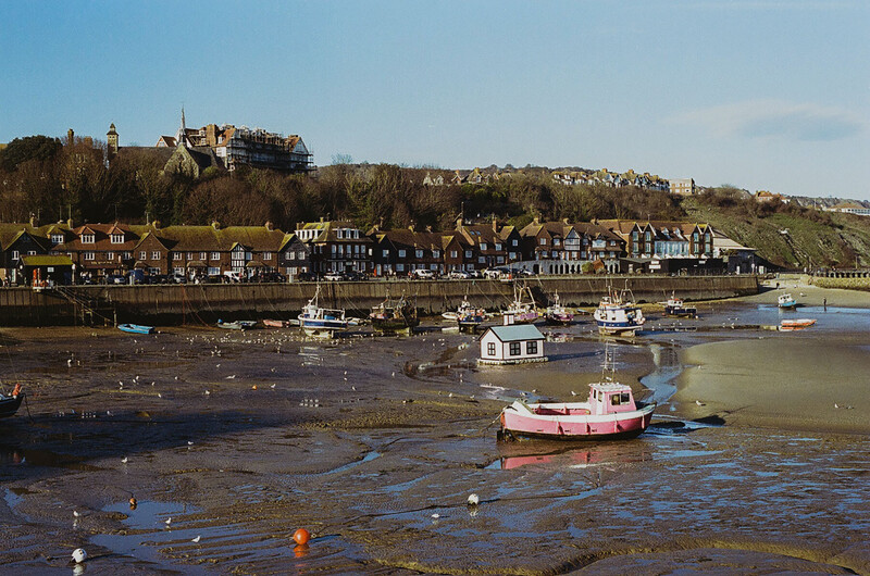 Coastal harbor at low tide with moored boats and traditional waterfront buildings on hillside