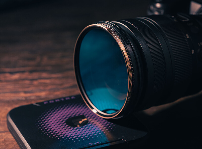 Camera lens with blue filter resting on illuminated RGB pad against warm wooden surface