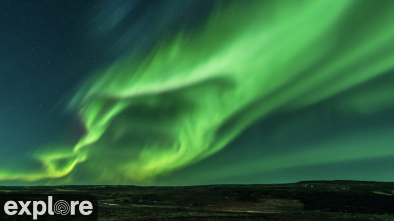 Vibrant green aurora borealis streaking across a dark night sky above a silhouetted landscape