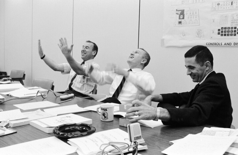 Three men in business attire at a conference table during what appears to be a 1960s office meeting or presentation