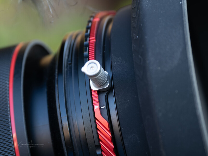Close-up of camera lens with red focus ring and metal adjustment knob
