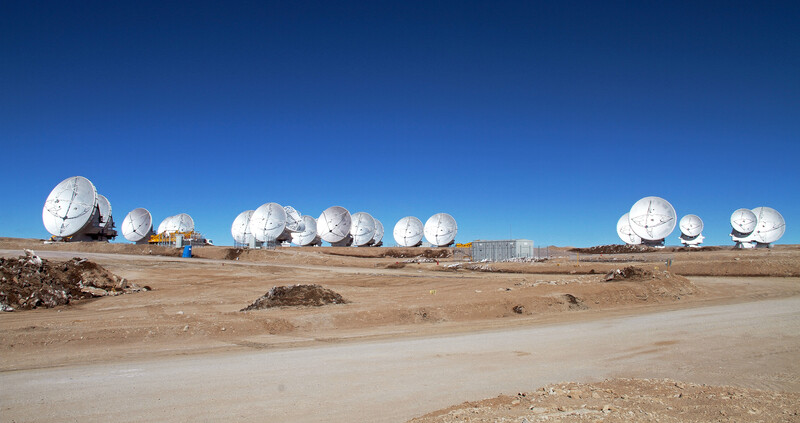 Large white satellite dishes arranged in a desert landscape under clear blue sky