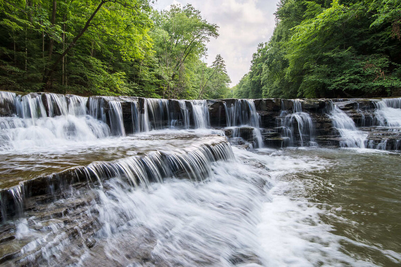 Tiered waterfall cascading through forested landscape with long exposure technique