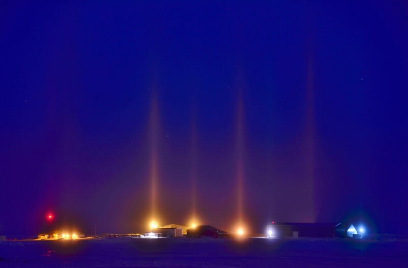 Night landscape with multiple light beams shooting upward from industrial structures against deep blue twilight sky