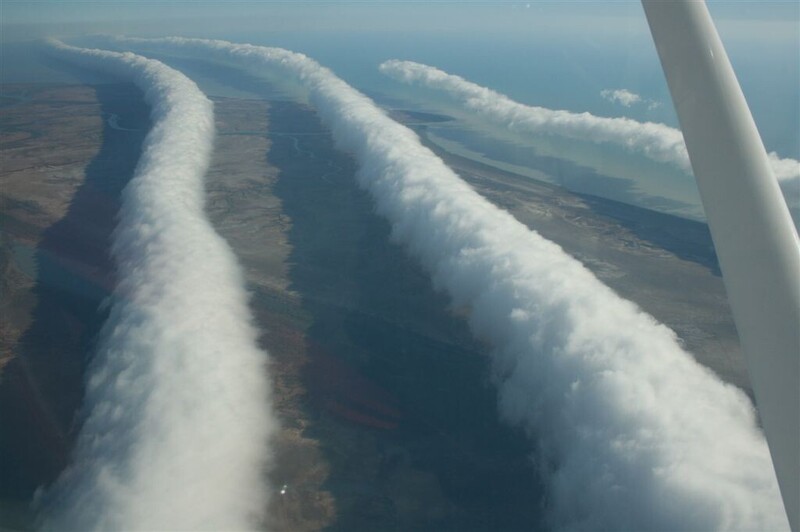 Aerial view of parallel contrails streaming from aircraft wing against landscape below