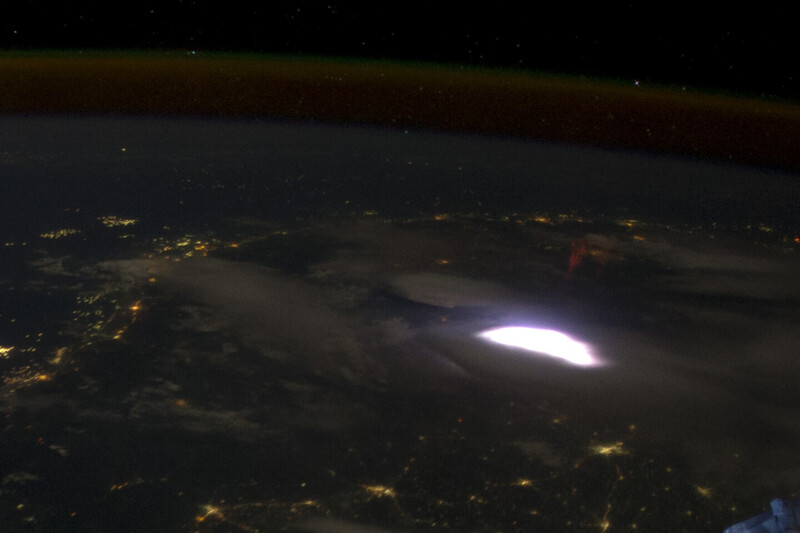 Lightning strike illuminating storm clouds above city lights at night from aerial perspective